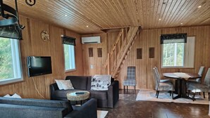 A cozy living room with a sofa, chairs, a coffee table, and a dining table with chairs. There is a staircase leading to another level, and a TV mounted on the wall. - Cabin-Garden view-Private Bathroom-Deluxe-Mökki 12,The Biggest Yell (Västerskog)
