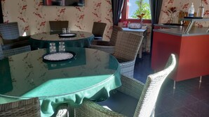 A dining area with round tables, wicker chairs, a flat-screen TV, and a kitchen area with a red counter and various items on shelves. - Cabin-Garden view-Private Bathroom-Deluxe-Mökki 12,The Biggest Yell (Västerskog)
