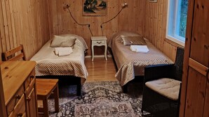 Una camera in una baita di legno con due letti, un tavolino, una sedia e un tappeto.
