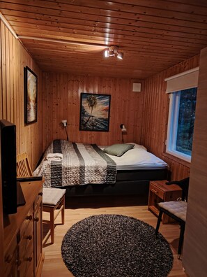 Ein gemütliches Schlafzimmer einer Holzhütte mit einem Bett, einem Schreibtisch und einem Fenster.
