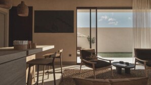 Una sala de estar moderna con un gran ventanal corredero que da a un área de piscina, un comedor con barra, y una zona de estar con una mesa de centro.