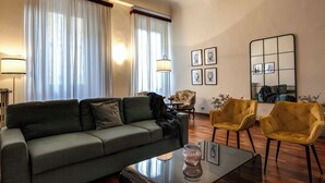 Un salon avec un canapé vert, deux fauteuils jaunes, une table basse en verre et un plancher en bois.