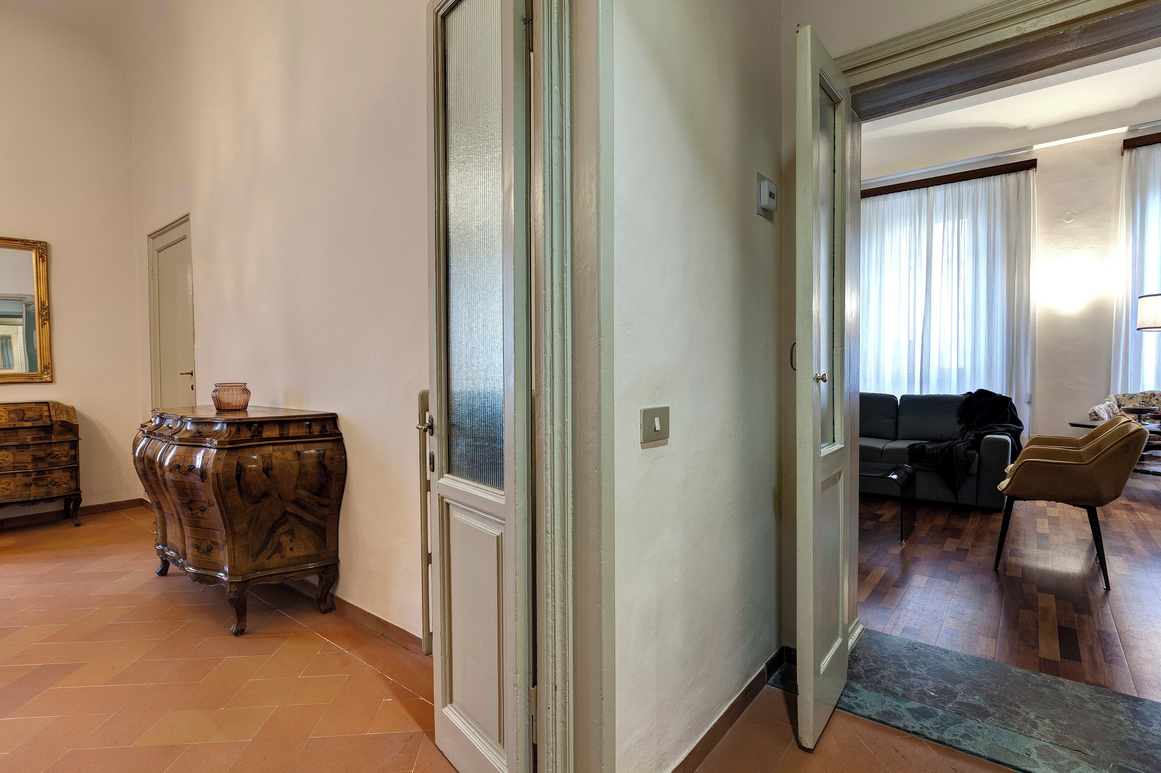A hallway with a wooden cabinet, a door, and a view into a living room with a sofa and a chair.