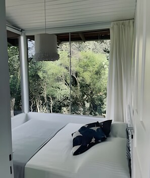 A bedroom with a large window, a bed, and a hanging light fixture. - Casa Fluila  (Imbituba)