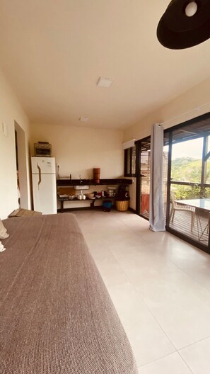 A room with a bed, a kitchenette, a dining area, and a large window with a view. - Casa Fluila  (Imbituba)