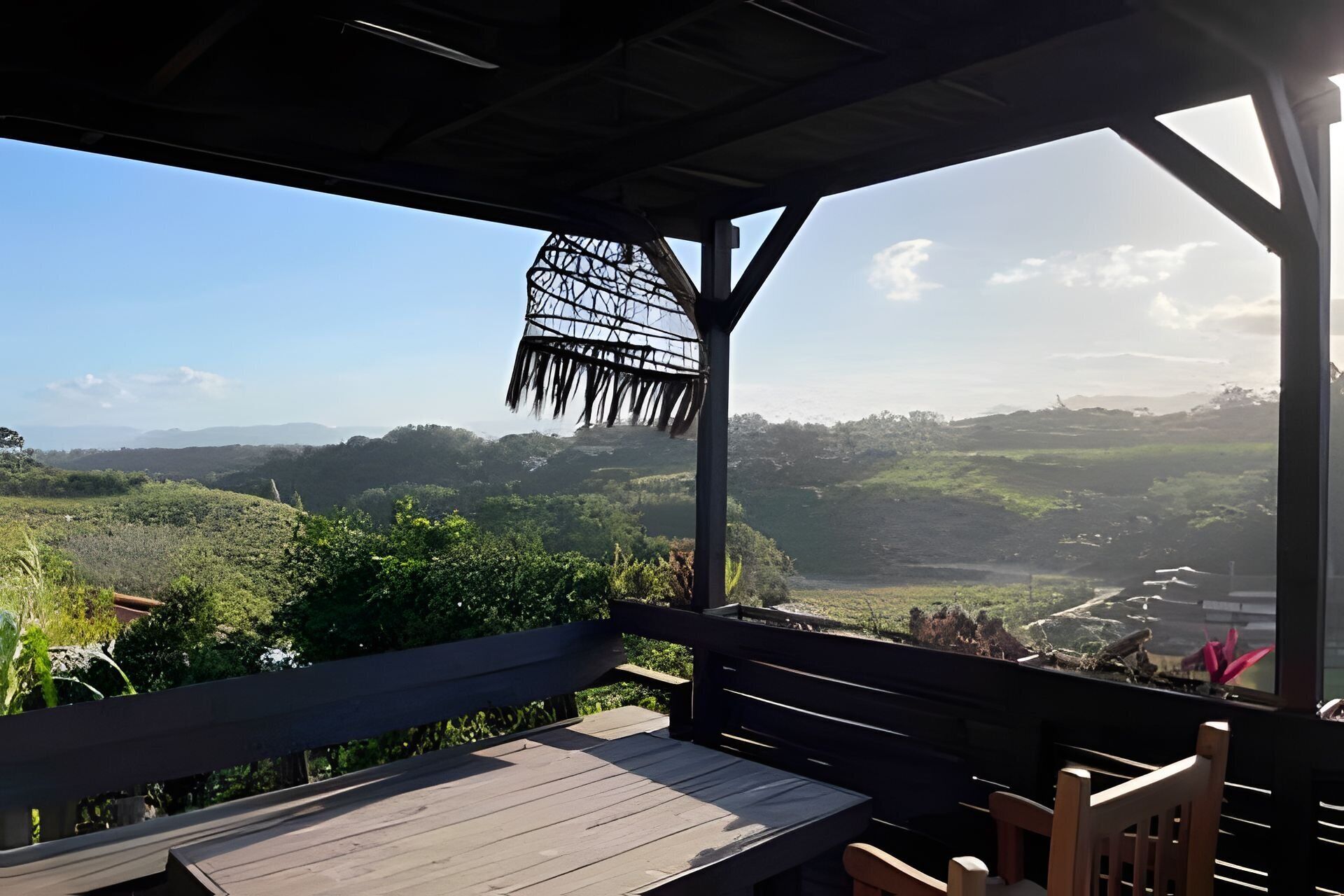 A wooden deck with a table and chairs, overlooking a lush landscape with hills and a clear sky.