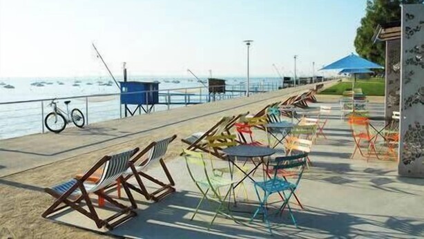 Un área de descanso junto a la playa con sillas y mesas, una bicicleta y una torre de salvavidas.