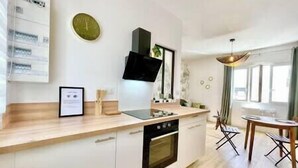 Una cocina moderna con horno empotrado, microondas y lavaplatos. Hay un comedor con mesa y sillas.