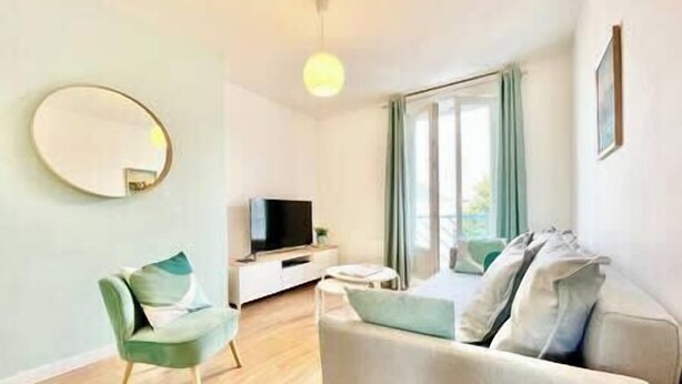 A modern living room with a sofa, a chair, a TV, and a large window with curtains.