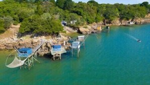 A coastal area with clear blue water, a wooden jetty with chairs, and a small building on the shore.