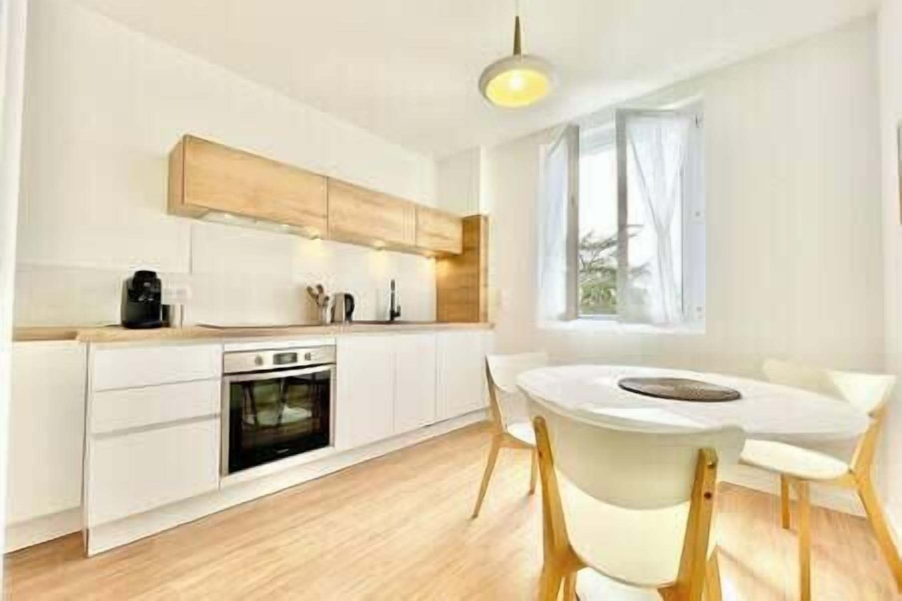 Una cocina moderna con armarios blancos, horno empotrado y una mesa de comedor con sillas de madera.
