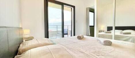 A hotel room with a large bed, a nightstand, a mirror, and a view of the balcony.