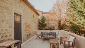 Un bâtiment en pierre avec une porte, une table entourée de chaises et une vue sur les arbres.