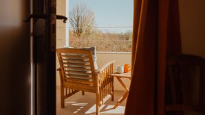 Une chaise et une table en bois sur un balcon, avec vue sur les arbres et un ciel dégagé.