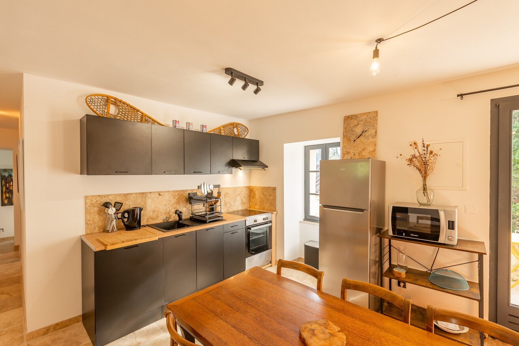Une cuisine compacte avec des meubles de couleur sombre, un plan de travail en bois, un four encastré, un réfrigérateur et un four à micro-ondes.