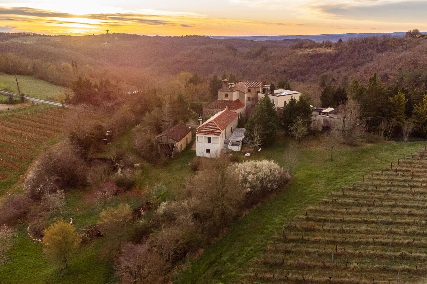 Un paysage rural avec une grande maison entourée de champs et d’arbres.