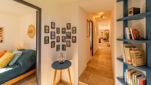 Un couloir comprenant un lit, une petite table avec une lampe, une bibliothèque et un mur orné de tableaux encadrés.