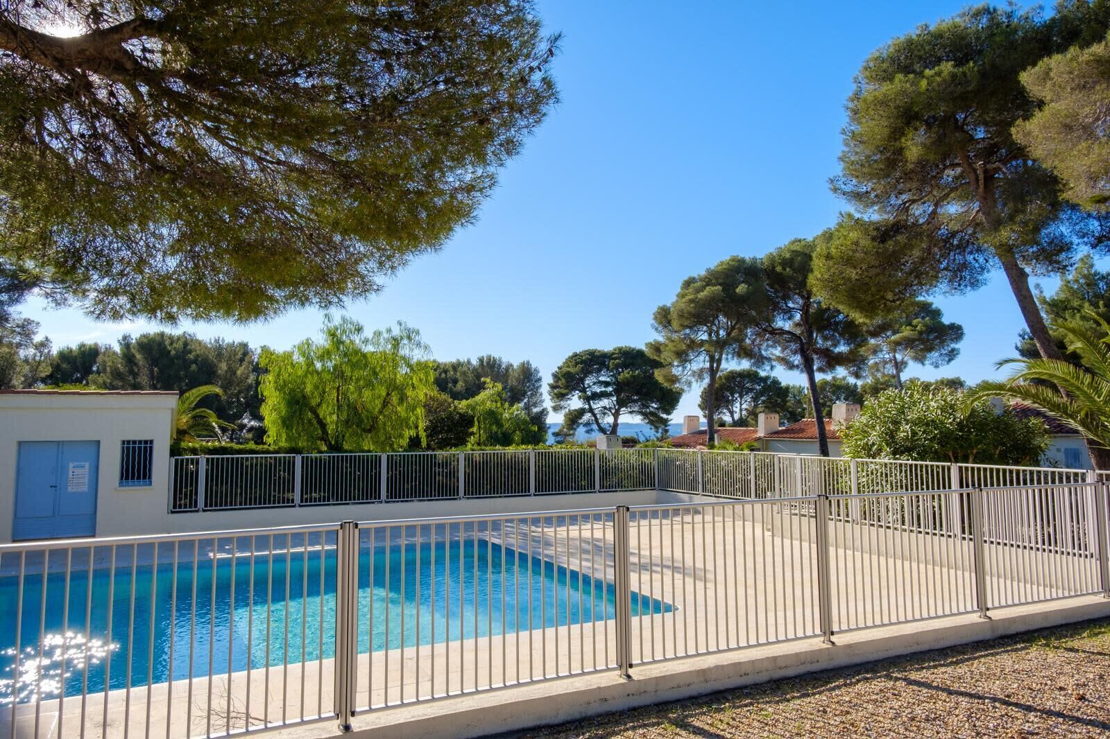 A swimming pool with a metal fence, surrounded by trees and buildings.