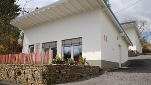 Un edificio moderno con fachada blanca, número 14, que presenta un muro de piedra, un camino de grava y una valla de madera.