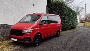 Una camioneta roja estacionada en un camino de grava junto a un edificio blanco con base de piedra y un seto verde.