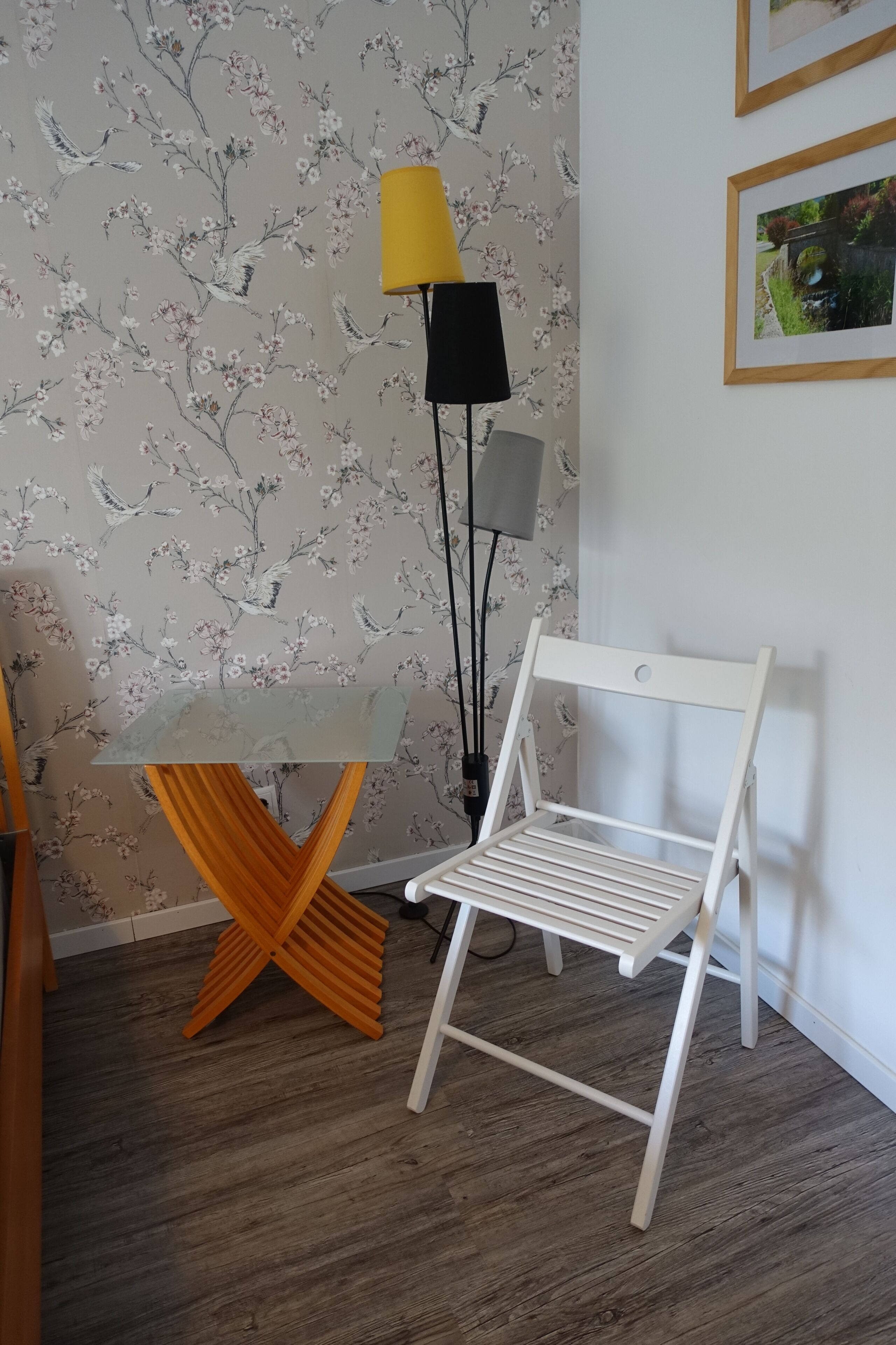 A room with a floral wallpaper, a white chair, a small table, and a floor lamp.