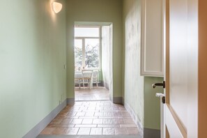 A hallway with a tiled floor, a door on the right, and a window at the end leading to an outdoor area with a table and chairs. - Appartamento delle Pietre (Cortona)