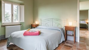 Ein Schlafzimmer mit Bett, Nachttischen, Heizkörper, Fenster und Tür.