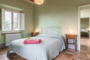 A bedroom with a bed, bedside tables, a radiator, a window, and a door. - Appartamento delle Pietre (Cortona)