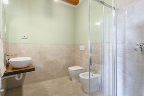 A bathroom with a glass shower enclosure, a white sink with a wooden countertop, and a white toilet. - Appartamento delle Pietre (Cortona)