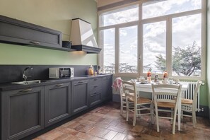 A kitchen with a window, cabinets, a microwave, and a dining table with chairs. - Appartamento delle Pietre (Cortona)