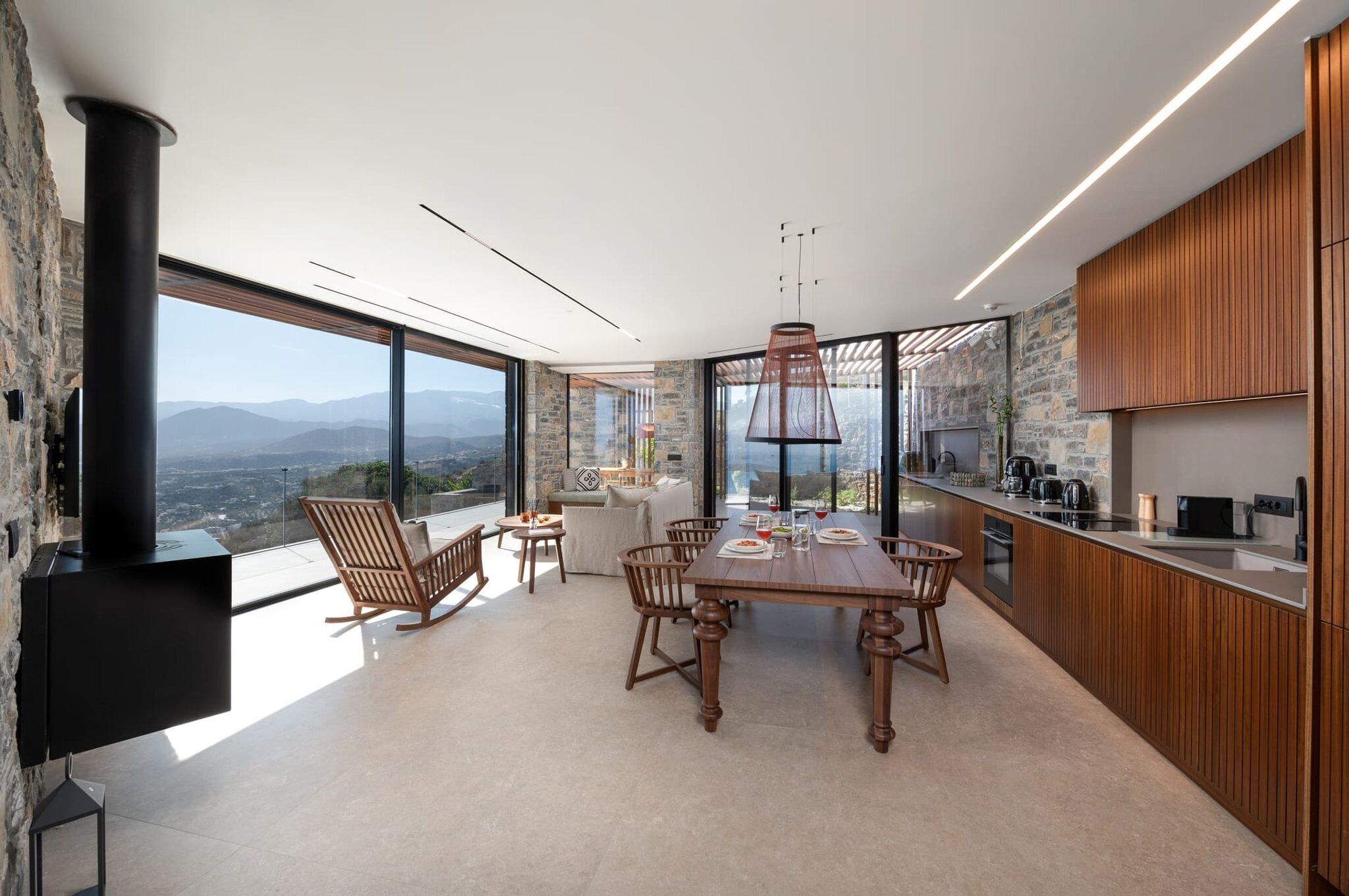 A modern kitchen with a large island, stone walls, and a view of the mountains.