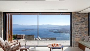 Un salon moderne doté d’une grande porte-fenêtre coulissante qui donne sur un balcon offrant une vue panoramique sur la mer et les montagnes.
