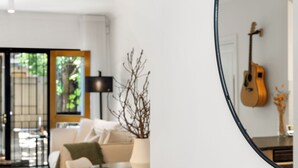 Un salon moderne avec une table basse en verre, un canapé et une lampe. On peut apercevoir une guitare dans le reflet du miroir.