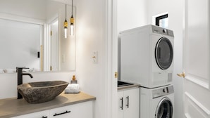 Une salle de bain moderne avec un lavabo en pierre, un miroir, un lave-linge et un distributeur de serviettes.