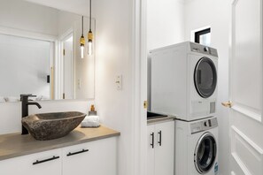 Une salle de bain moderne avec un lavabo en pierre, un miroir, un lave-linge et un distributeur de serviettes.