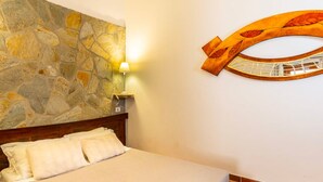 A bedroom with a stone wall, a wooden headboard, a bed with white linens, and two wall-mounted lamps. - Room 'Mirto' with Mountain View, Wi-Fi and Air Conditioning (Uta)