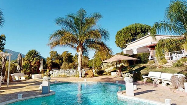 A pool area with palm trees, lounge chairs, and a building with a white facade. - Room 'Mirto' with Mountain View, Wi-Fi and Air Conditioning (Uta)