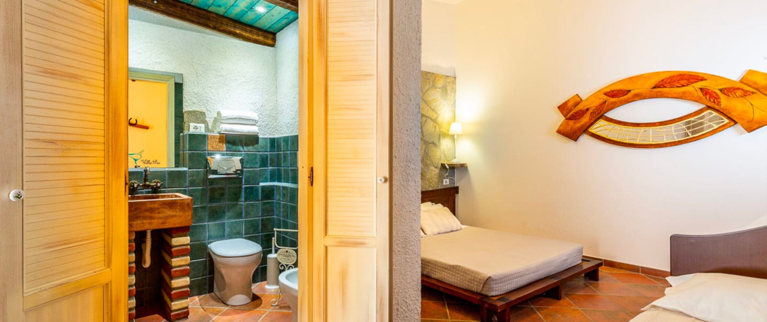 Quarto com cama, porta de madeira, banheiro com vaso sanitário e pia.