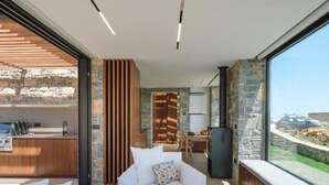 Interior moderno com sofá branco, área de cozinha e janela grande com vista para carro e paisagem.