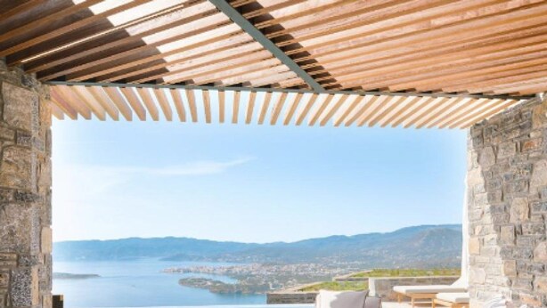 Uma área de estar ao ar livre luxuosa, com vista para uma cidade costeira e montanhas.