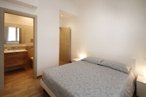 A bedroom with a bed, bedside tables, a wooden door, and a bathroom visible through an open door.