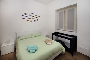 A neatly arranged bedroom with a green bedspread, a bedside table with a lamp, and a window with blinds. - Aunt's house-just a stone's throw from the sea (Marina di Caronia)