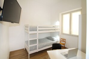 Une chambre avec un lit superposé, un bureau et une chaise, un ordinateur portable et un téléviseur fixé au mur.