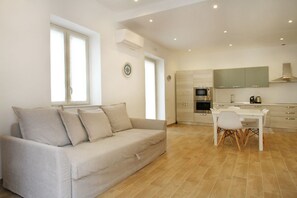 A modern living room with a beige sofa and a dining area with a white table and chairs.
