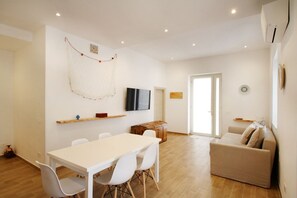 Un salon moderne avec un canapé blanc, une table à manger avec des chaises, un téléviseur fixé au mur et un meuble en bois.