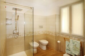Un baño con ducha de vidrio, un bidé, un inodoro y un perchero con una toalla.