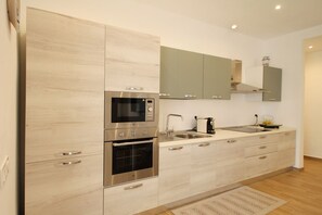 Une cuisine moderne dotée d’appareils électroménagers en acier inoxydable, de meubles de rangement en bois clair et d’un four encastré.