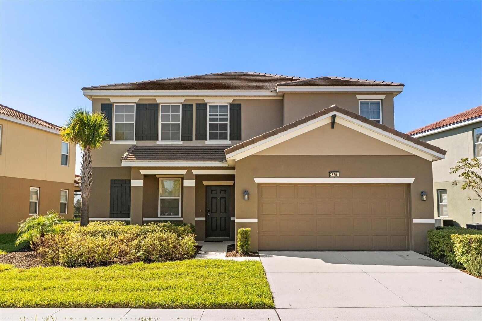 A two-story residential building with a front garage, a well-maintained lawn, and a clear blue sky.