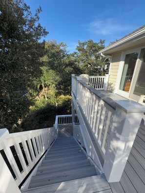 A wooden staircase leading to a deck with white railings, surrounded by trees and a house with a window. - Escape to beautiful Brightside OBX-Your Corolla Outer Banks Beach Retreat Awaits (Corolla)