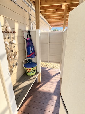 Eine Holzterrasse mit einer Bank, einem Eimer und einem an der Wand befestigten Regal mit Muscheln.